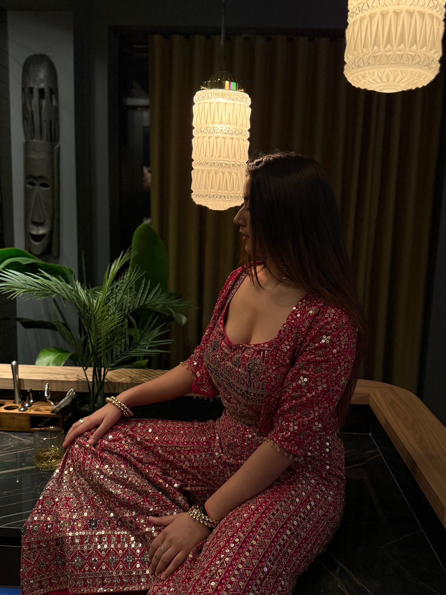 Woman in a red patterned dress sitting in a dimly lit room with hanging lights.