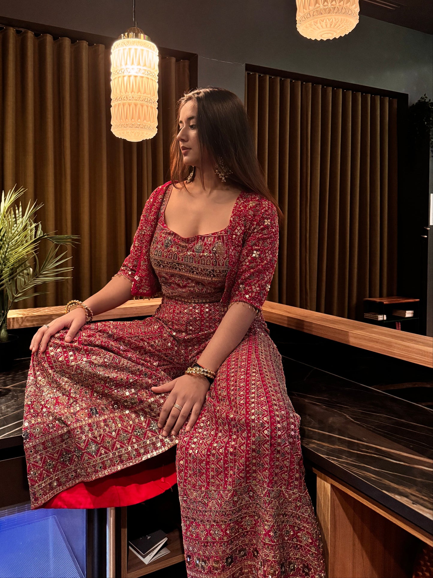 Woman in a red and gold traditional outfit standing in a room with decorative elements.
