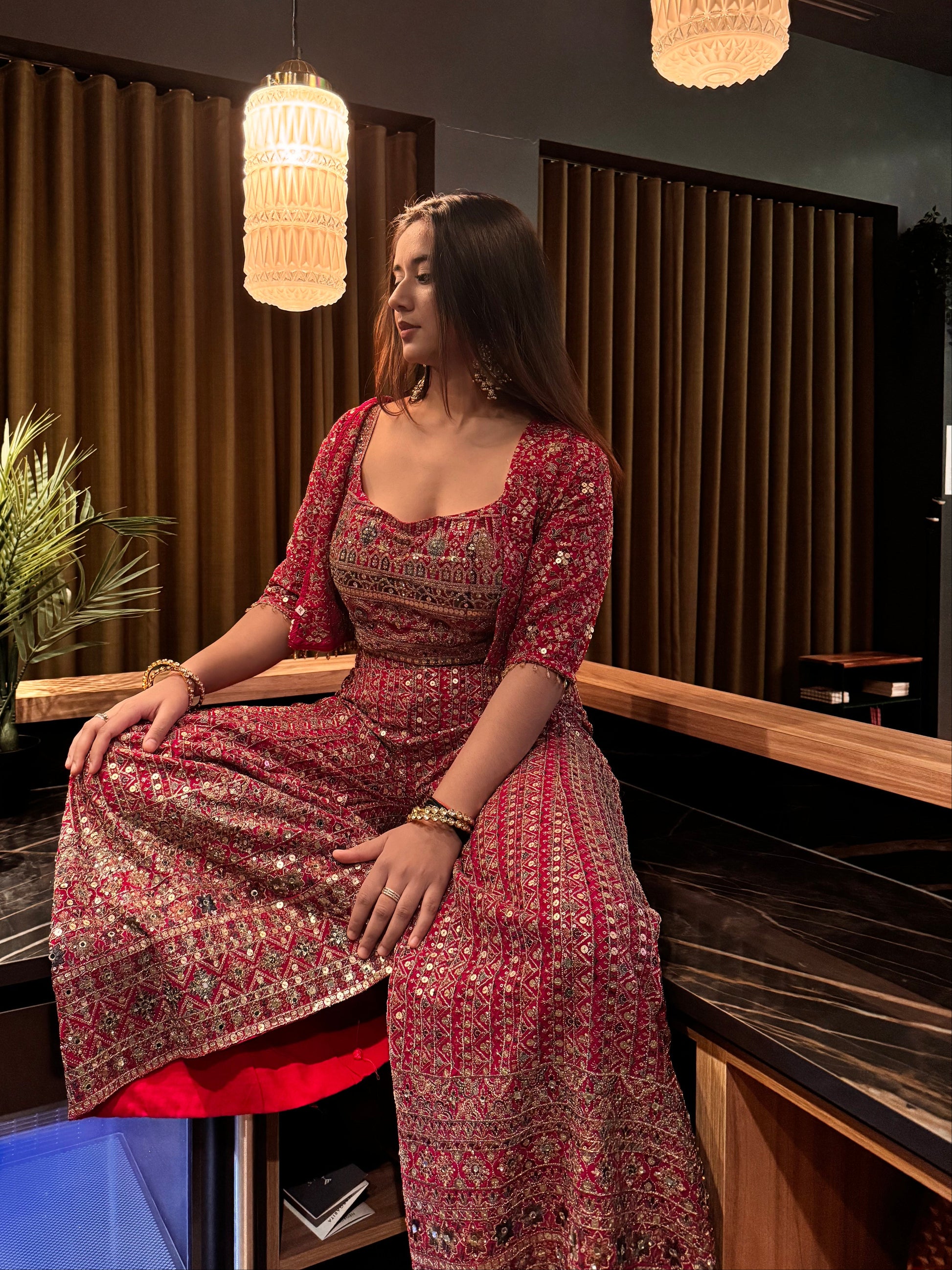 Woman in a red and gold traditional outfit standing in a room with decorative elements.