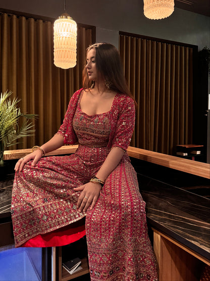 Woman in a red and gold traditional outfit standing in a room with decorative elements.