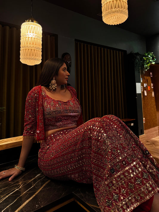 Woman in a red and gold traditional outfit sitting on a marble bench in a dimly lit room.